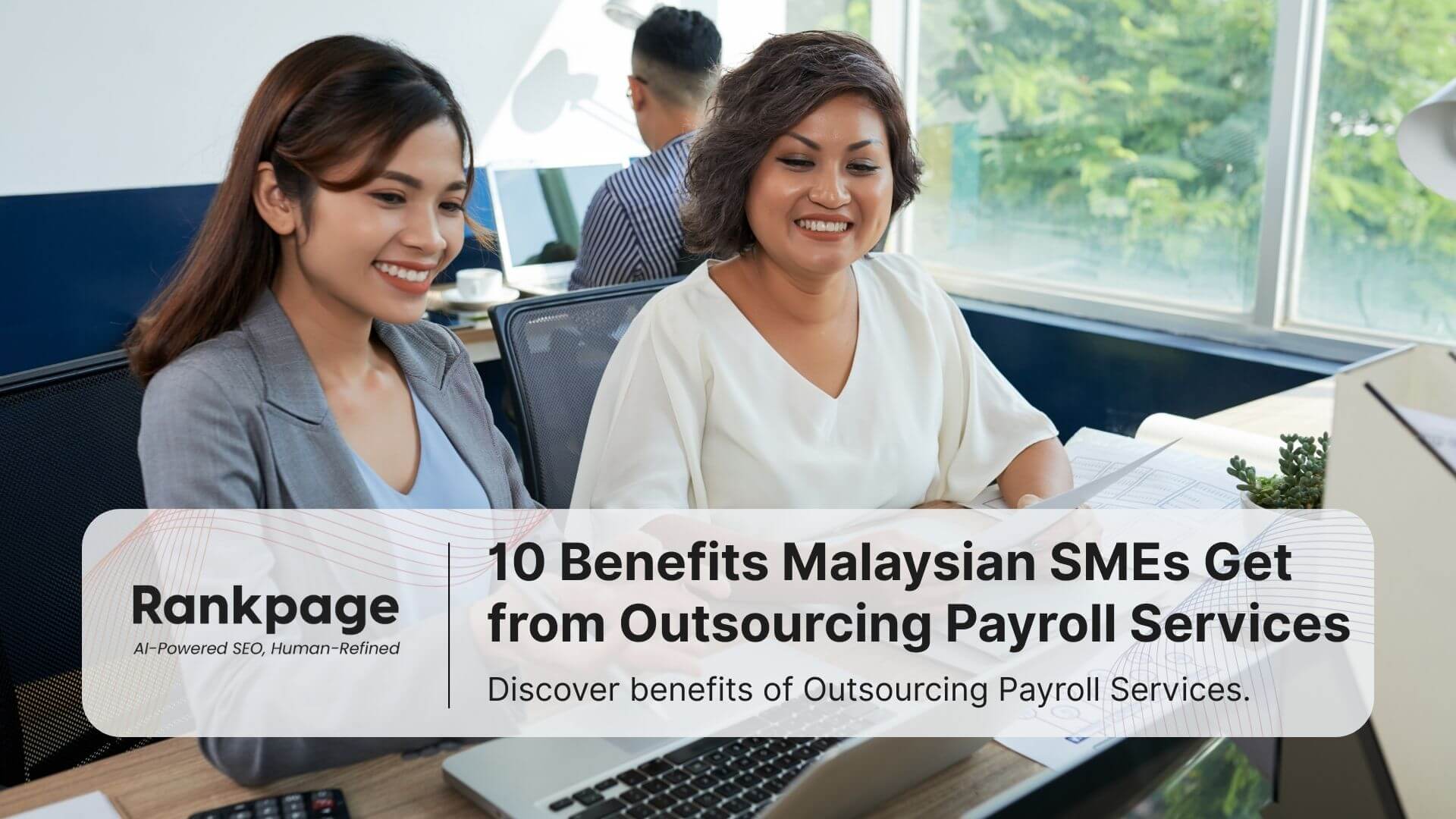 two-asian-female-colleagues-sitting-at-office-desk-with-laptop-helping each-other-smiling